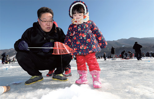 인제빙어축제에서 한 어린이가 아빠와 함께 빙어낚시를 즐기고 있다