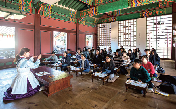 약첩 싸기 체험이 이루어지는 창덕궁 약방 전경. 체험에 참여한 사람들이 약재의 특징과 효능에 대한 설명을 듣고 있다.