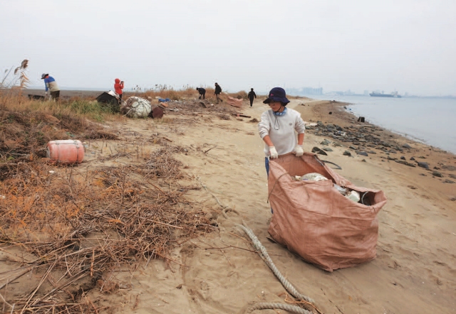 서천군 지속가능발전협의회 회원들이 바다 쓰레기를 담은 마대를 옮기고 있다. 남쪽 해변으로 넘어오는 다리가 좁아 사람이 직접 마대를 날라야 한다.