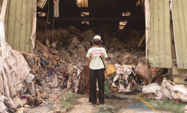 홍다경 대표가 쓰레기 더미 위에서 ‘쓰레기산 OUT’이라고 쓴 종이상자 피켓을 들고 있다. 