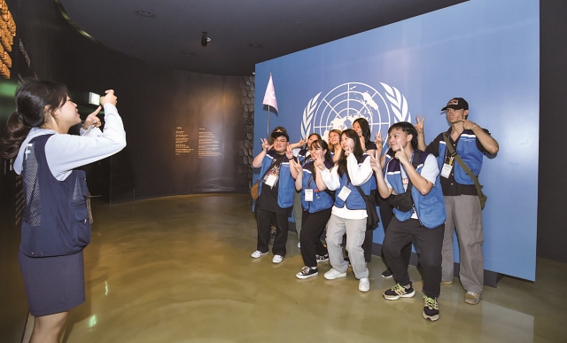 전쟁기념관을 찾은 ‘2023 유엔참전용사 후손 교류캠프’ 참가자들이 유엔 국기 앞에서 기념촬영을 하고 있다. 사진 C영상미디어