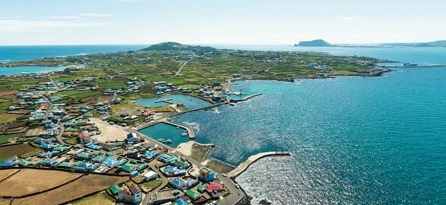 돌담과 알록달록한 지붕이 어우러진 우도는 때묻지 않은 자연 그대로의 제주를 보여준다. 우도 뒤로 제주 본섬의 성산일출봉이 보인다.