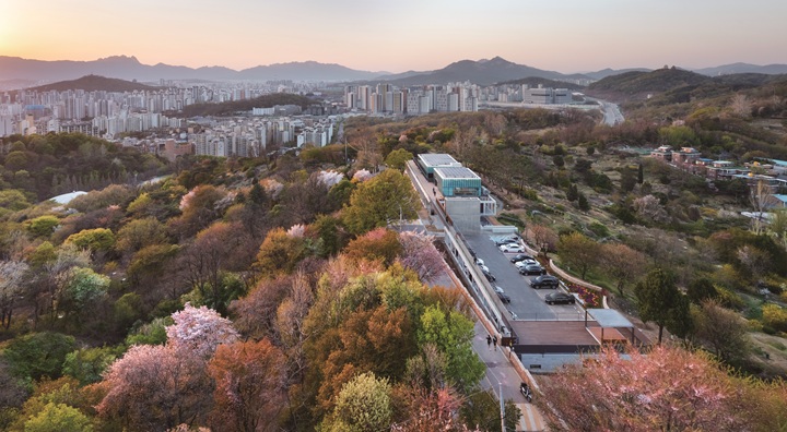 중랑망우공간을 위에서 내려다본 모습. 능선 위에 얕은 건물이 조용히 놓여 있고 그 주변으로 묘역과 숲이 우거져 있다. 사진 건축사진가 박영채