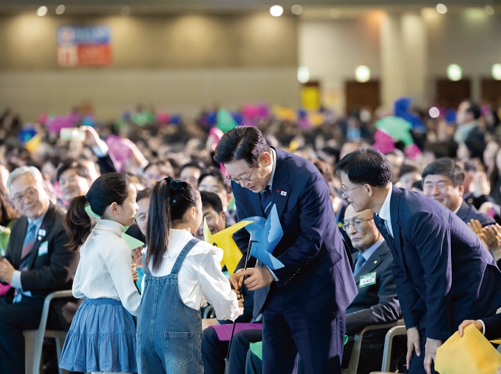 이재명 대통령이 12월 2일 경기 고양시 킨텍스에서 열린 &lsquo;제22기 민주평화통일자문회의 출범회의&rsquo;에서 어린이들로부터 국민의 바람을 뜻하는 바람개비를 전달받고 있다. 사진 대통령실
