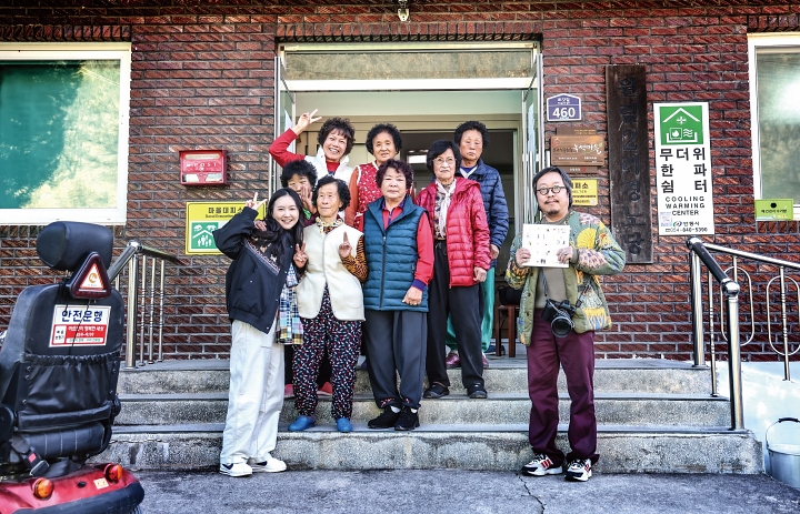 ‘로컬그라피 오월’ 소속 최민지 활동가와 이재각 사진가가 2025년 12월 1일 오후 토갓마을 마을회관 앞에서 마을 어르신들과 함께 포즈를 취하고 있다. 사진 C영상미디어