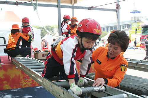 비상탈출로 교육을 받는 아이가 한걸음씩 조심스럽게 사다리를 건너고 있다.