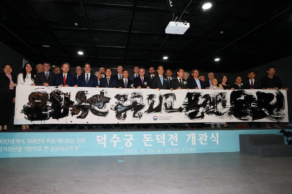 한덕수 국무총리가 25일 서울 중구 덕수궁 내 재건된 돈덕전 개관식에 참석해 붓글씨 퍼포먼스로 만든 현수막을 들고 참석자들과 기념촬영을 하고 있다.
