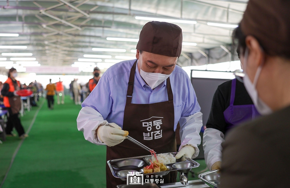 윤석열 대통령이 27일 서울 명동성당 내 무료 급식소인 ‘명동밥집’에서 봉사활동을 펼치며 식판에 음식을 담고 있다.