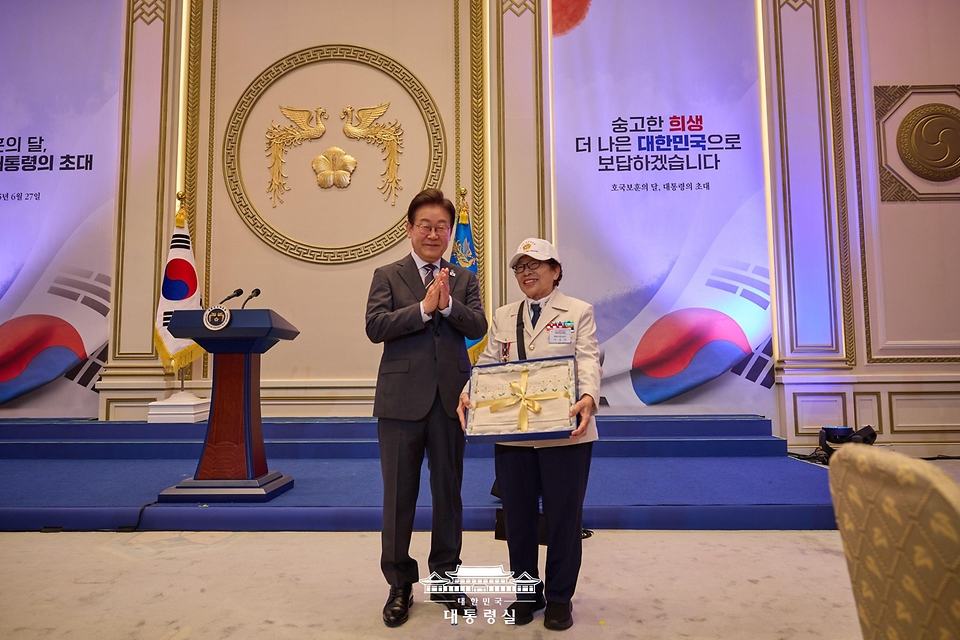 이재명 대통령이 27일 청와대 영빈관에서 열린 '호국 보훈의 달, 대통령의 초대' 행사에서 특별 초청대상자인 이춘자 씨에게 광목이불을 선물한 뒤 박수치고 있다.