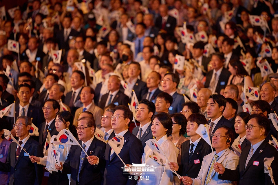 이재명 대통령과 김혜경 여사가 15일 서울 세종문화회관에서 열린 80주년 광복절 경축식에서 참석자들과 함께 태극기를 흔들며 광복절 노래를 제창하고 있다.