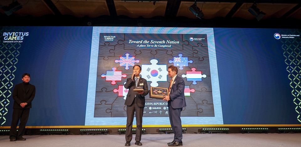 권오을 국가보훈부 장관이 2월 26일 오후 서울시 중구 더플라자호텔에서 열린 인빅터스재단 실사단 방한 만찬에 참석해 롭 오웬 재단 대표와 함께 유치 의지 전달 퍼포먼스를 하고 있다.