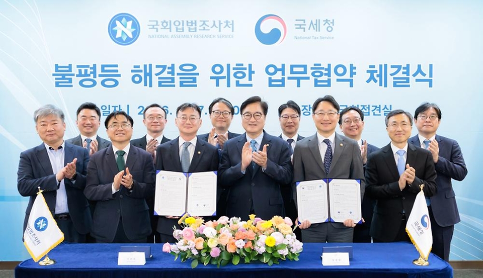 임광현 국세청장이 4월 17일 국회접견실에서 열린 불평등 해결을 위한 국세청-국회입법조사처 업무협약 체결식에서 협약서에 서명을 하고, 우원식 국회의장, 이관후 국회입법조사처장을 비롯한 관계자들과 기념촬영을 하고 있다.