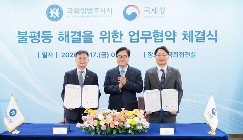 임광현 국세청장이 4월 17일 국회접견실에서 열린 불평등 해결을 위한 국세청-국회입법조사처 업무협약 체결식에서 협약서에 서명을 하고, 우원식 국회의장, 이관후 국회입법조사처장을 비롯한 관계자들과 기념촬영을 하고 있다.