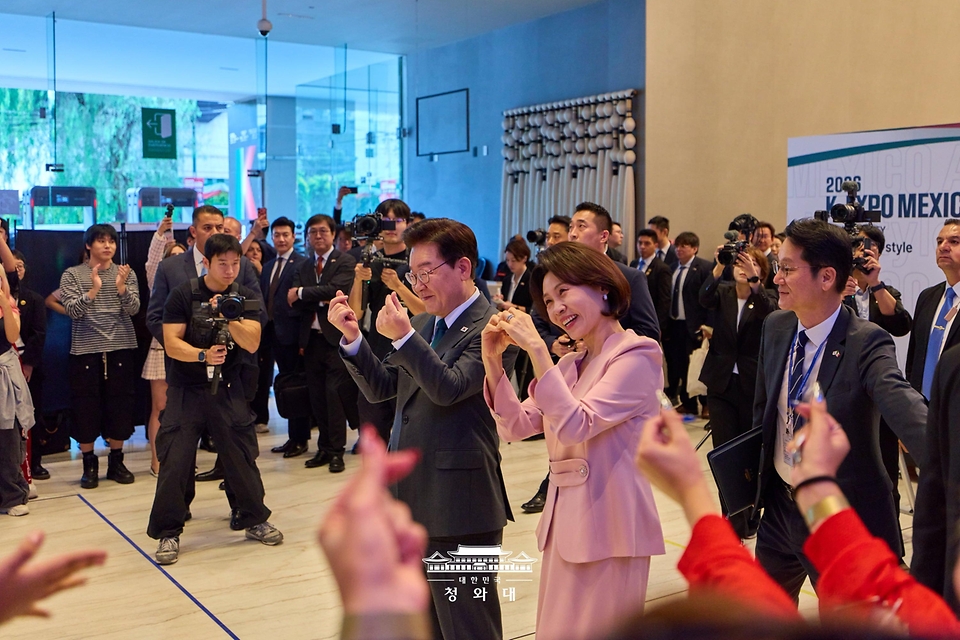 이재명 대통령과 김혜경 여사가 9월 25일(현지 시간) 멕시코시티 세계무역센터(WTC)에서 열린 랜덤 플레이 댄스 행사에서 참가자들을 향해 하트를 만들어 보이며 인사하고 있다.