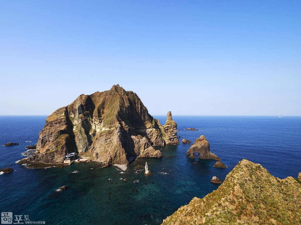 독도는 동도(東島)·서도(西島) 및 그 주변에 흩어져 있는 89개의 바위섬으로 이루어져 있다. 사진에서는 서도와 촛대처럼 생긴 촛대바위, 탕건처럼 생긴 바위 탕건봉, 3개의 굴이 있어 이름붙여진 삼형제굴바위가 보인다. 