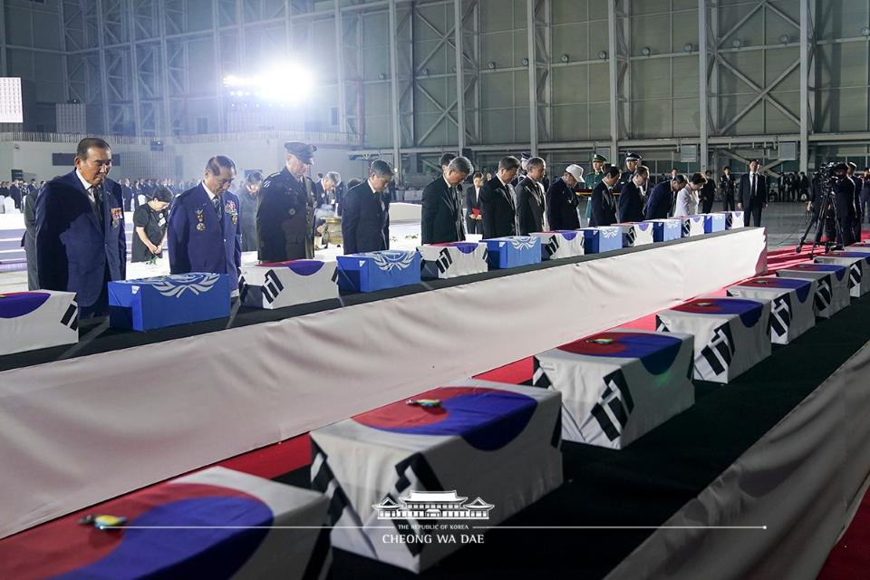 문재인 대통령이 25일 경기 성남 서울공항에서 열린 6.25전쟁 70주년 행사에서 국군 전사자들의 유해함에 참전기장을 수여한뒤 참석자들과 묵념하고 있다.