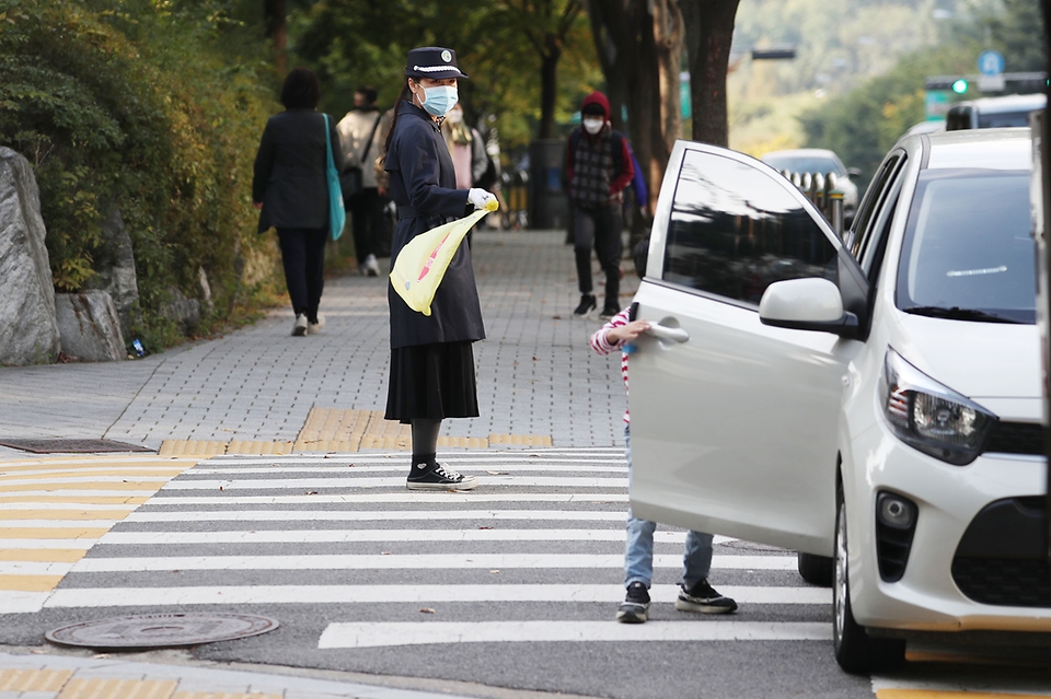 개정 도로교통법이 첫 시행된 21일 오전 서울 마포구 한 초등학교 인근 '어린이 통학 차량 안심 승·하차존에서 한 학부모가 교통 지도를 하고 있다. 서울시는 시내 학교 정문이나 후문과 인접한 곳에 '어린이 통학 차량 안심 승·하차존'을 운영한다. 오늘(21일)부터 어린이보호구역(스쿨존) 내 모든 도로에서 차량 주·정차가 전면 금지된다.  