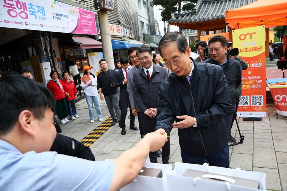 한덕수 국무총리가 20일 서울 종로구 통인시장을 방문해 상인들을 격려하고 구매 영수증으로 사은행사에 참여하고 있다.