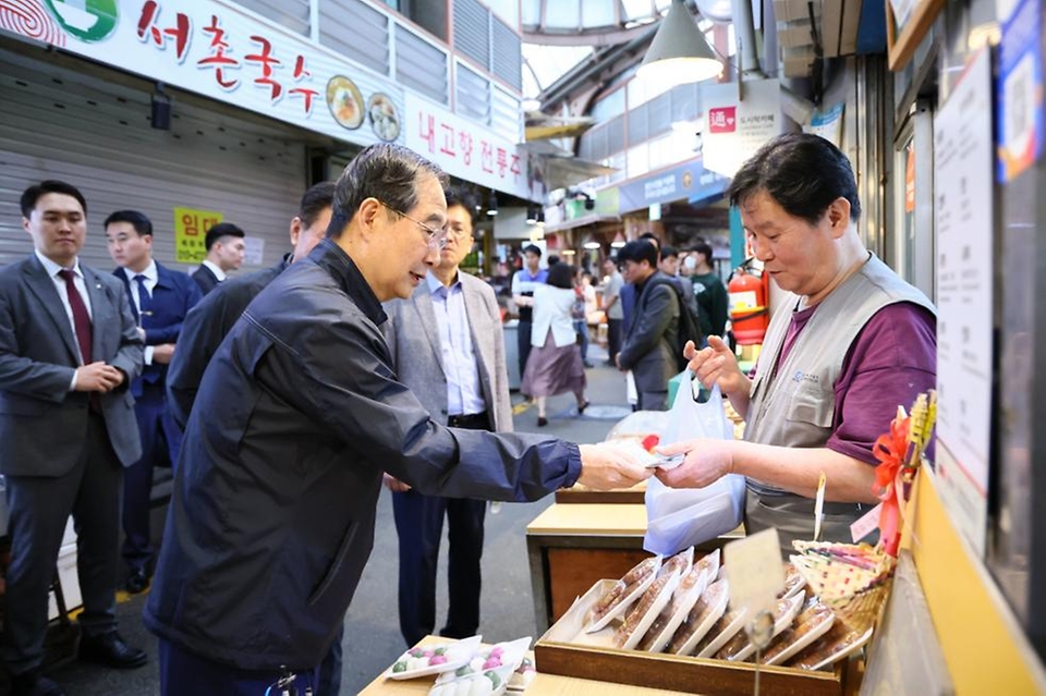 한덕수 국무총리가 20일 서울 종로구 통인시장을 방문해 점포를 돌아보며 떡을 구매하고 있다.