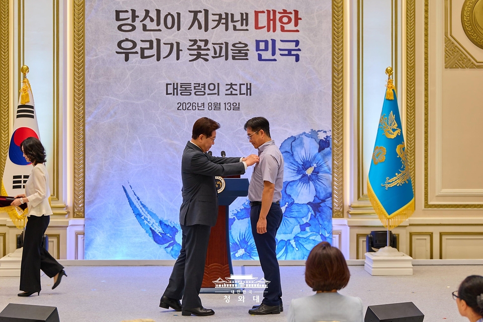 이재명 대통령이 8월 13일 청와대 영빈관에서 열린 국가유공자 및 보훈 가족 초청 오찬에서 2023년 혹한기 훈련 중 사망한 고 최민서 일병 부친 최재우씨에게 태극기 배지를 달아주고 있다.