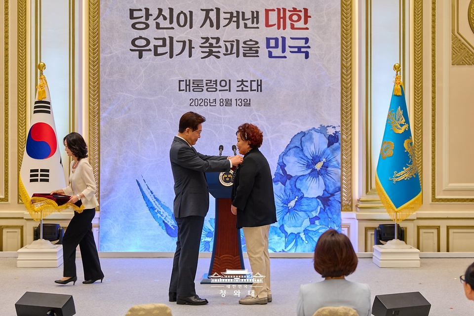 이재명 대통령이 8월 13일 청와대 영빈관에서 열린 국가유공자 및 보훈 가족 초청 오찬에서 5·18민주유공자 고 정동년 선생의 배우자 이명자 씨에게 태극기 배지를 달아주고 있다.