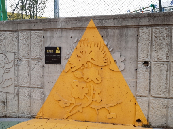 횡단보도 입구에 어린이들이 대기하는 옐로 카펫이 삼각형 모양으로 벽과 바닥에 그려져있다.