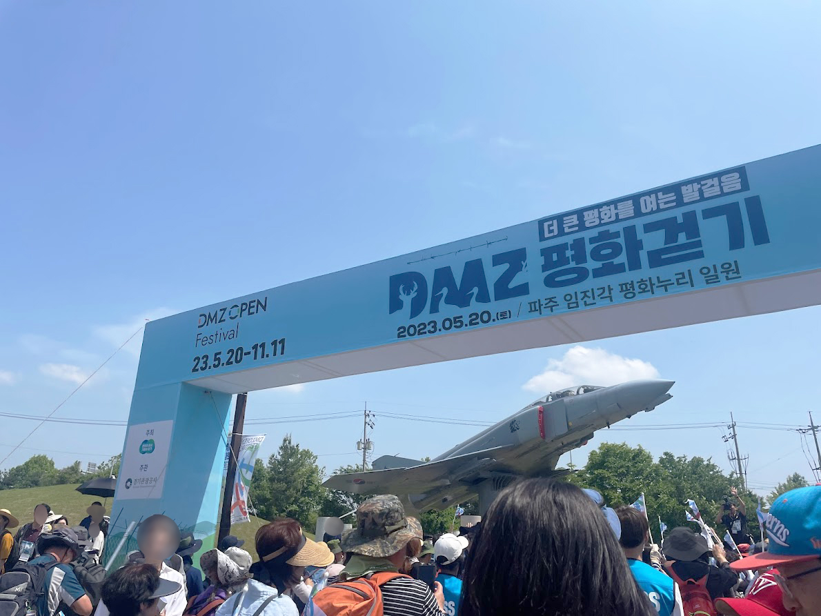 파란 하늘 아래 "DMZ 평화걷기"의 출발점인 안내판이 있다. 많은 사람들이 출발 신호를 기다리고 있다.