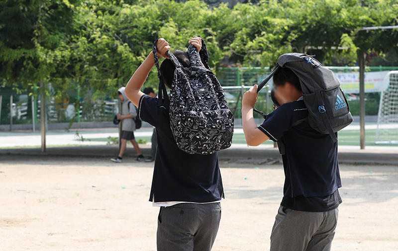 단축수업을 마친 학생들이 가방으로 태양을 피하고 있다. (사진=저작권자(c) 연합뉴스, 무단 전재-재배포 금지)