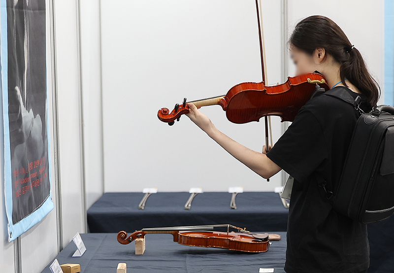 지난 8월 대구 북구 엑스코에서 열린 ‘대구 국제 악기&음향기기박람회’에서 관람객들이 전시된 바이올린을 시연해보고 있다. (사진=저작권자(c) 연합뉴스, 무단 전재-재배포 금지)