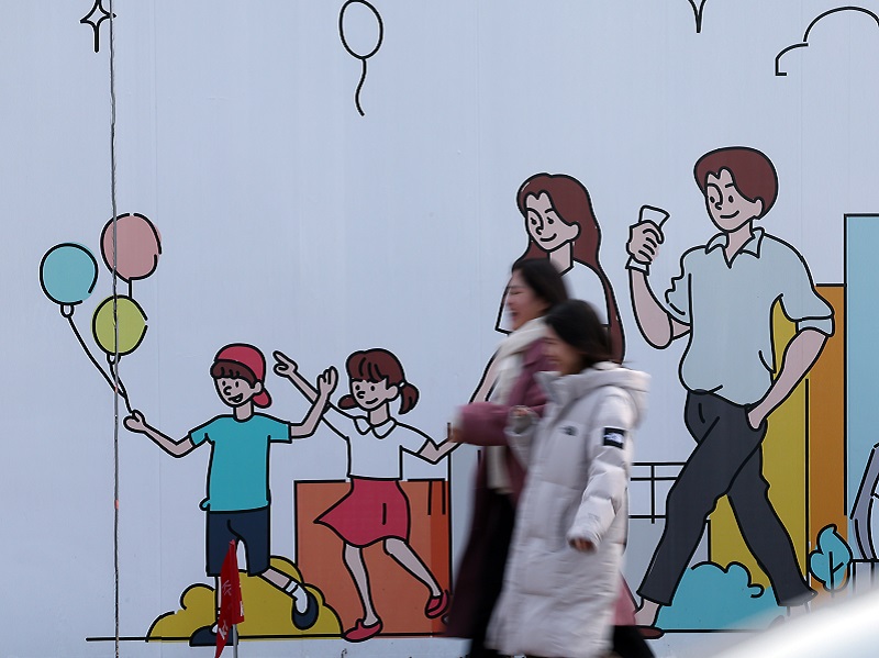 서울 도심의 공사장 가림막에 그려진 행복한 가족 그림 앞으로 시민들이 지나고 있다. 2024.1.29. (ⓒ뉴스1, 무단 전재-재배포 금지)