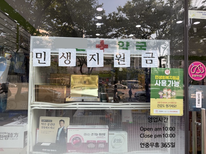 약국의 유리창에 소비쿠폰을 사용할 수 있다는 내용의 포스터와 안내 문구가 붙어 있는 모습.