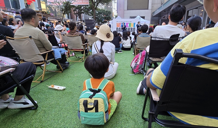 어린아이가 바닥에 앉아 공연을 감상하고 있다.