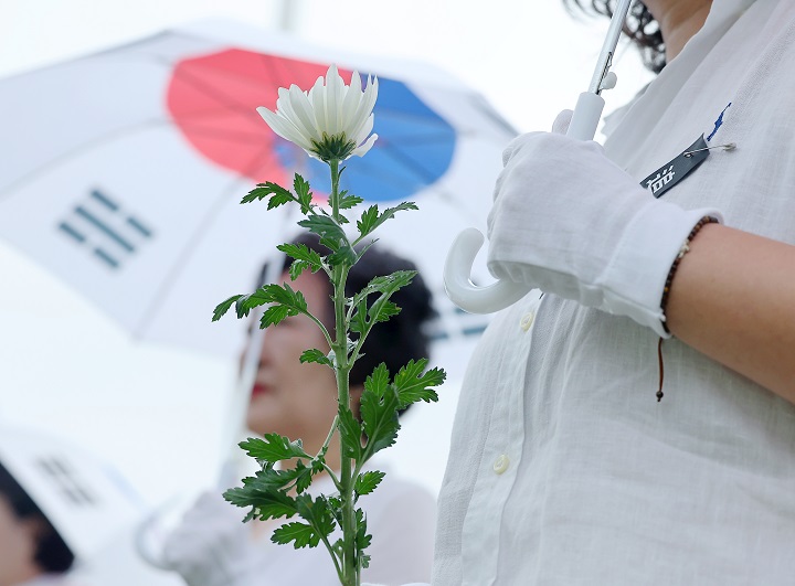 6·25전쟁 75주년인 25일 오전 부산 남구 유엔기념공원에서 열린 6·25전쟁 참전 유엔군 전몰용사 추모제에서 태극기 우산을 쓴 참석자들이 상징구역에 헌화할 국화꽃을 들고 있다. 2025.6.25(저작권자(c) 연합뉴스, 무단 전재-재배포 금지)