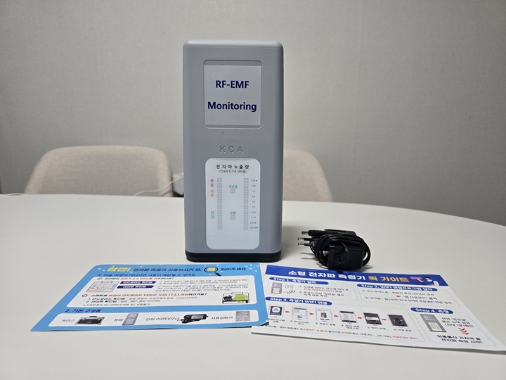 구성품으로는 소형 전자파 측정기, 전원 어댑터, 두 장의 안내문이 들어 있다.