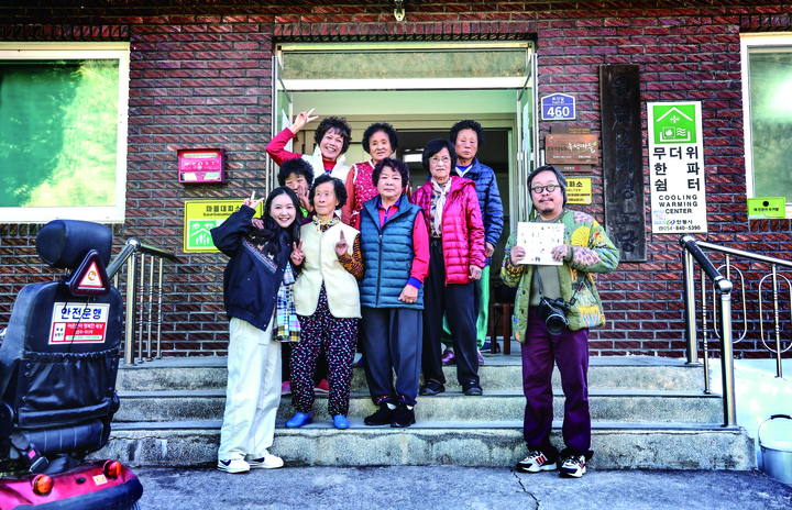 '로컬그라피 오월' 소속 최민지 활동가와 이재각 사진가가 2025년 12월 1일 오후 토갓마을 마을회관 앞에서 마을 어르신들과 함께 포즈를 취하고 있다.