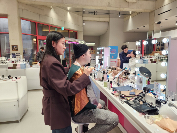 외국인 남성이 전문가의 설명을 들으며 퍼스널 컬러 진단을 받고, 자신의 피부 톤과 어울리는 색에 대해 조언을 듣고 있다.