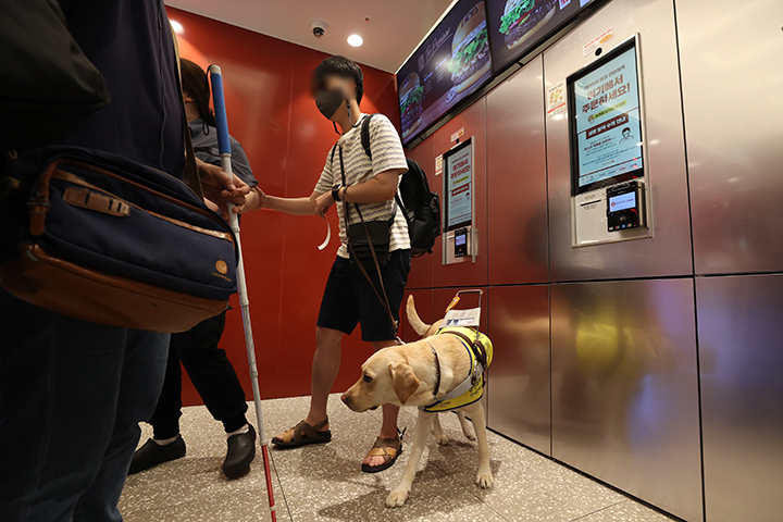 시각장애인들이 12일 서울의 한 패스트푸드점을 찾아 무인주문기(키오스크)에서 실제 주문을 해보는 '내돈내산 권리찾기 캠페인'을 하고 있다. 사진은 한 참가자가 직원의 도움으로 좌석으로 이동하는 모습. 2022.7.12 (사진=저작권자(c) 연합뉴스, 무단 전재-재배포 금지)