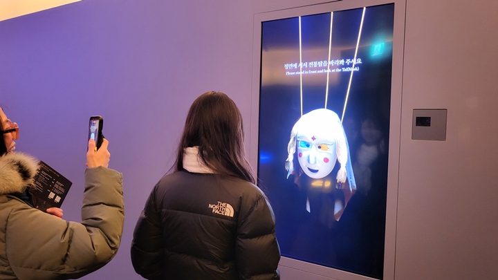 관람객이 전통 탈 앞에서 고개를 움직이며 탈춤 흉내를 내고 있다.