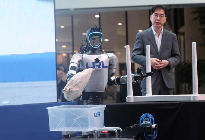 13일 대전 유성구 KAIST 본원 KI빌딩에서 열린 '피지컬 AI 코리아 2026'에서 명현 전기및전자공학부 교수 연구팀의 휴머노이드 '지원'이 음성 명령을 받아 테이블 위 파우치를 사족 보행 로봇 '테리'에 옮기고 있다. 2026.10.13 (사진=저작권자(c) 연합뉴스, 무단 전재-재배포 금지)