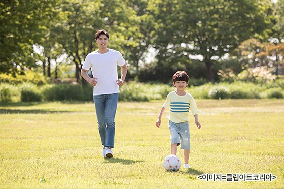 햇살 아래서 축구하고 있는 아빠와 아들.